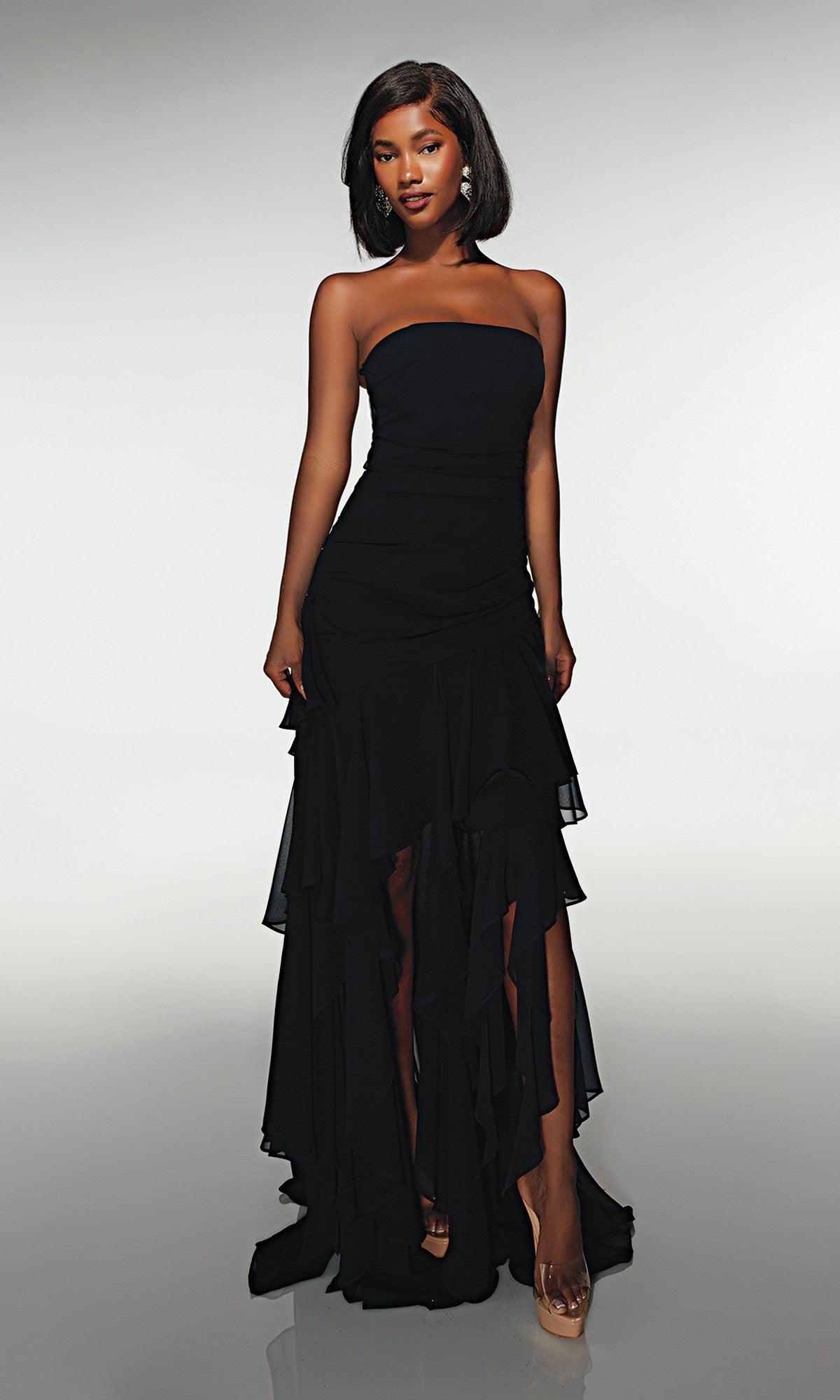 A woman stands against a light background in the Alyce 62153 long formal dress in midnight, featuring ruffled details and paired with nude heels.